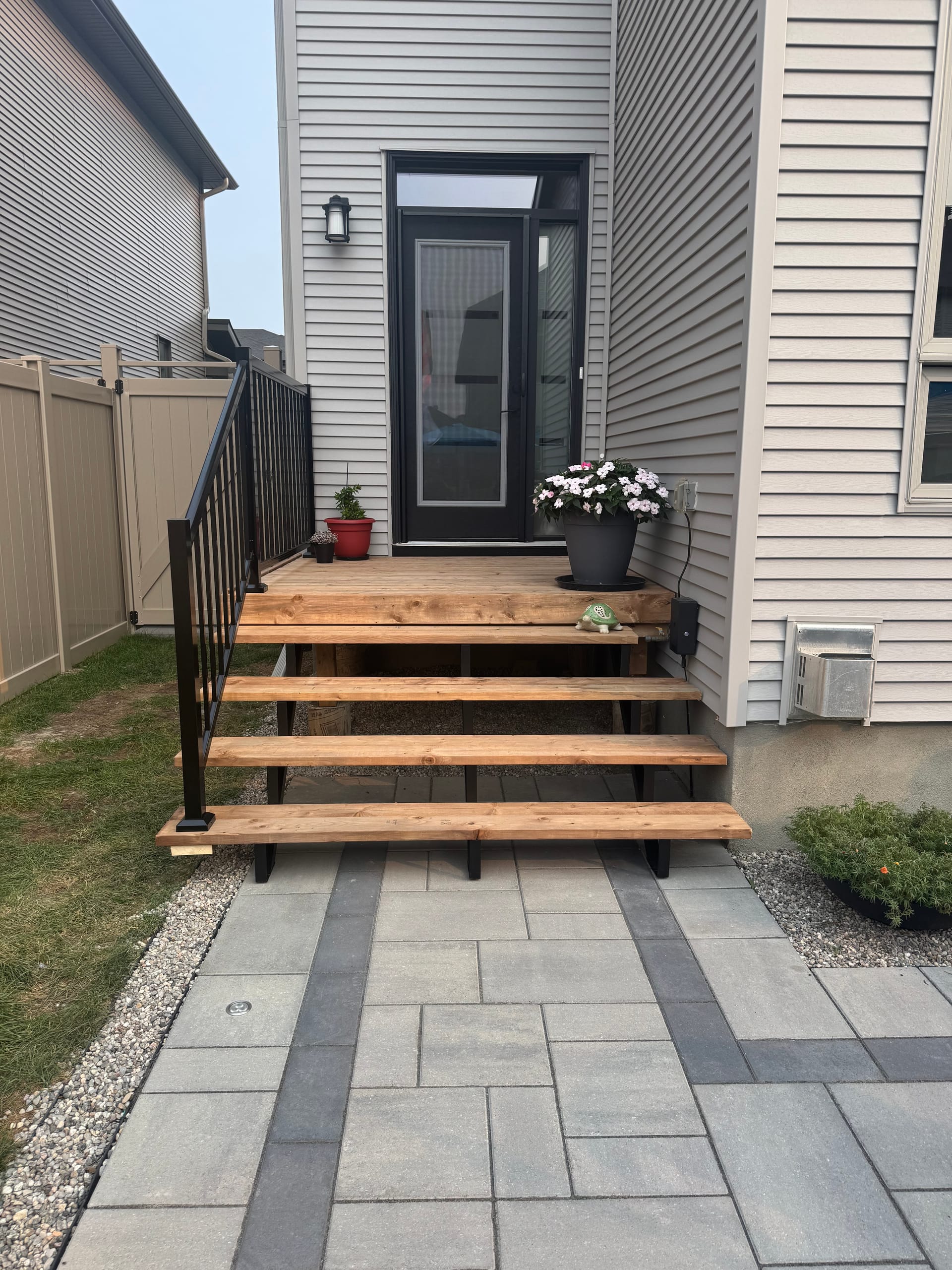 Wood deck stairs with black aluminum railings over interlock patio