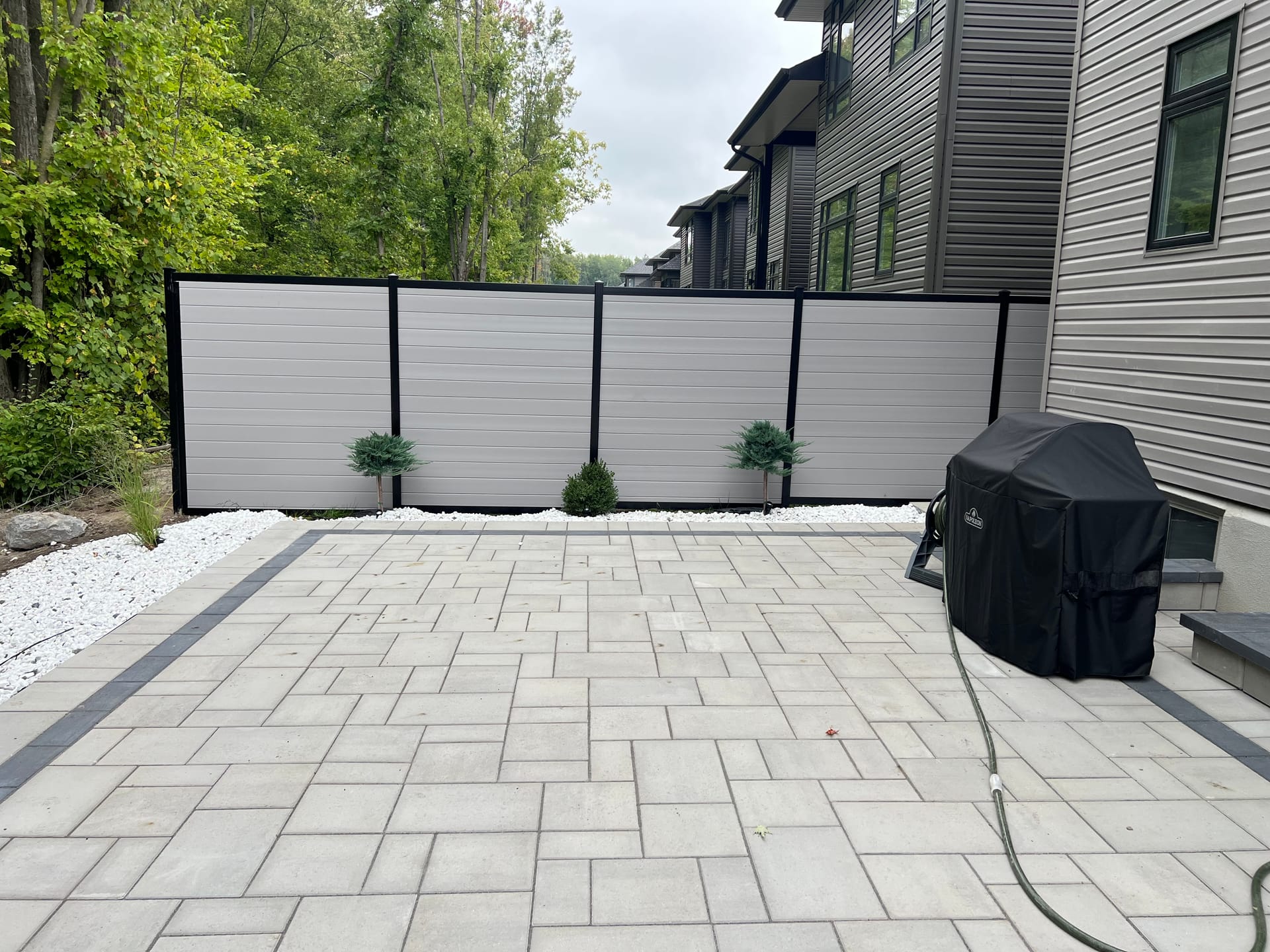 Modern hybrid grey fence with black posts and interlock patio