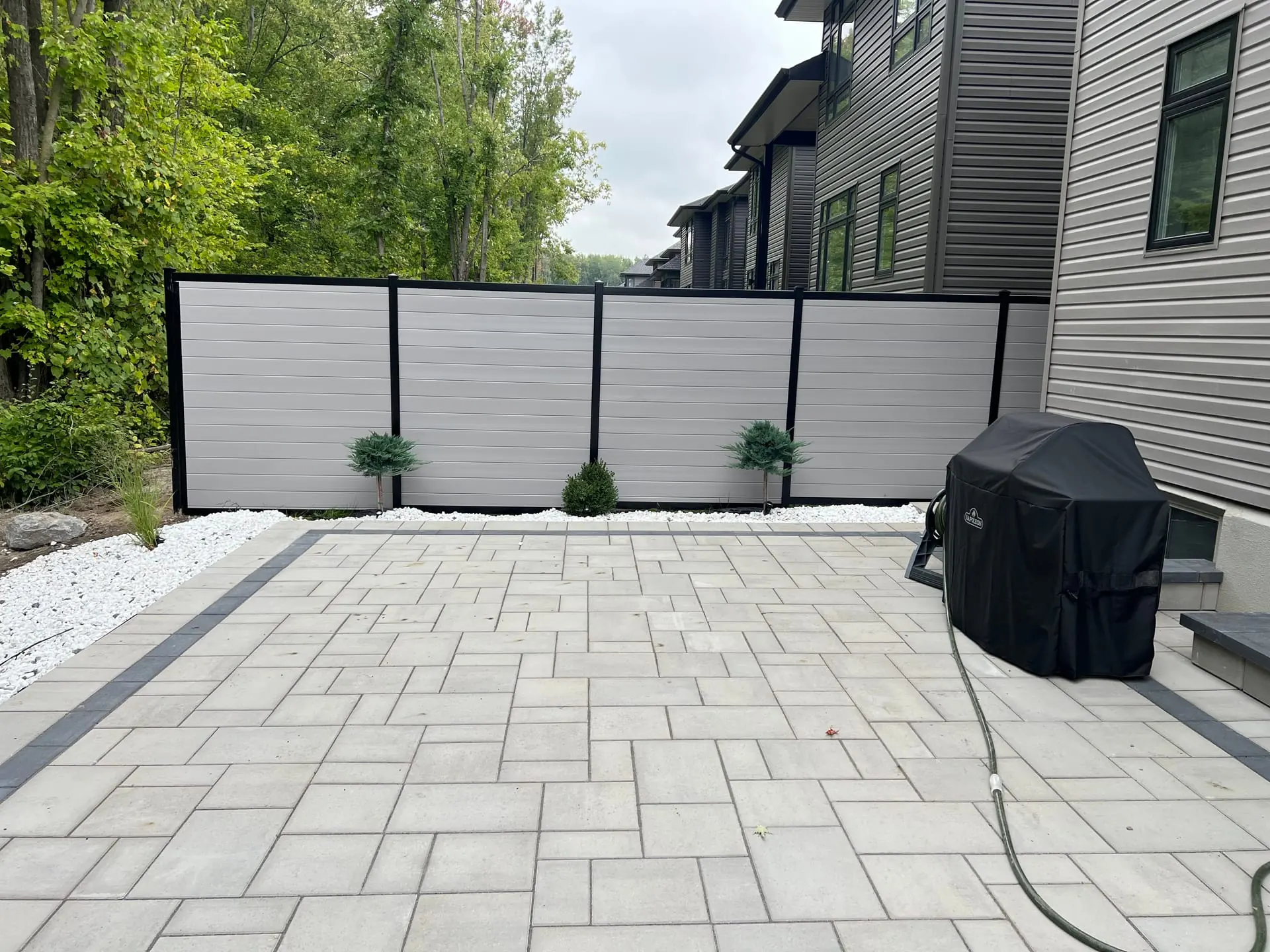 Modern hybrid grey fence with black posts and interlock patio